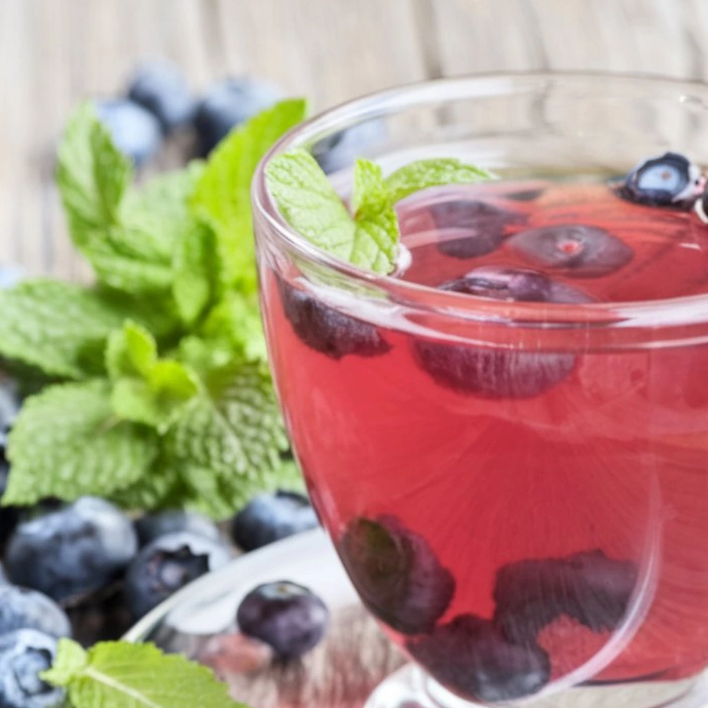 A glass of blueberry-infused herbal tea garnished with mint leaves, surrounded by fresh blueberries and mint sprigs.